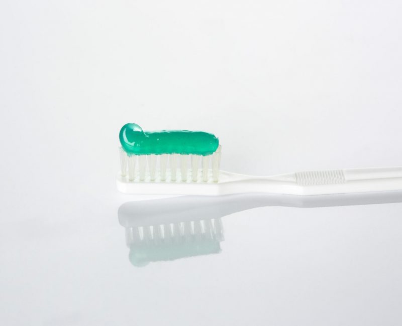 White plastic toothbrush with green gel toothpaste. Mint or spearmint flavor. Close-up of the bristle.