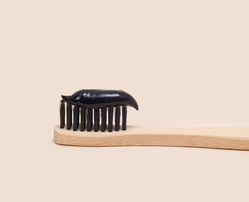 Black toothpaste on a bamboo brush with black bristles on a beige background. Minimalism. Dental health care